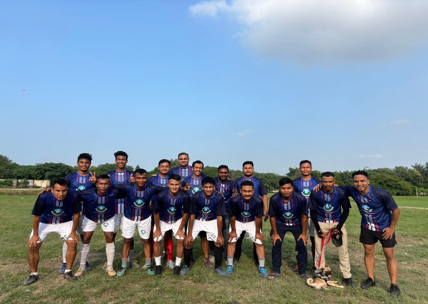 Group of male athletes in soccer kit posing for team photo on outdoor football ground with blue sky.